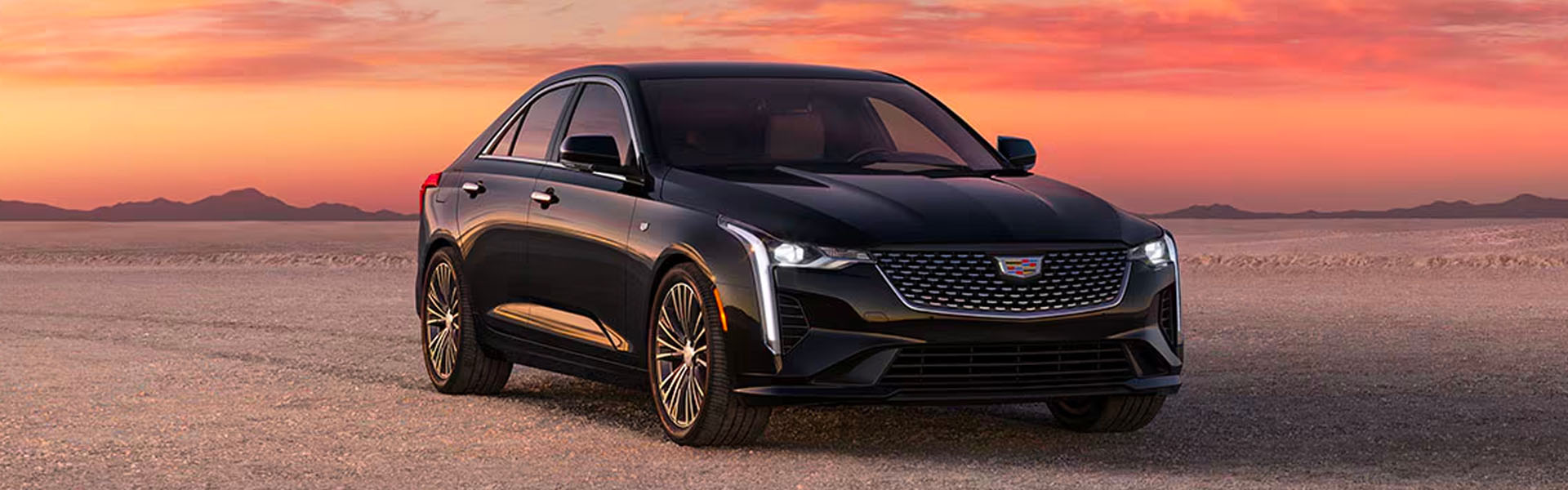 2025 Cadillac CT4 black luxury sedan parked on an open desert landscape at sunset