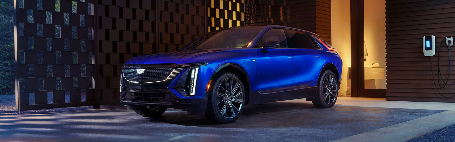 A blue 2026 Cadillac LYRIQ parked in front of a modern home with a car charging station.
