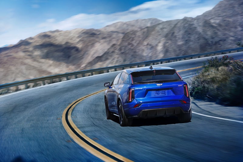 Rear View of a Blue 2026 OPTIQ-V Driving on a Curve of a Mountain Row | AutoNation Cadillac West Palm Beach in West Palm Beach FL